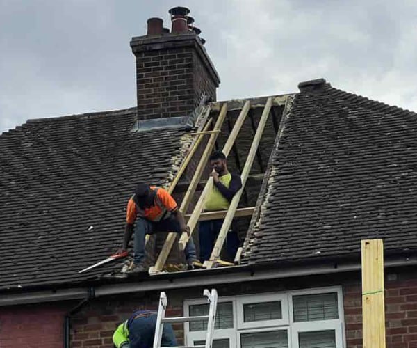 This is a photo of a roof repair being carried out. A section of the roof has been stripped and two roofers are replacing the rafters. Works being carried out by KAM Roofing Askern